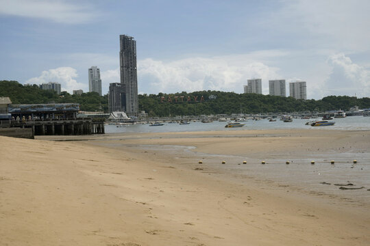 view of pattaya beach during low tide featuring sandy shoreline, anchored boats, modern city skyline, and dramatic monsoon clouds over the gulf of thailand