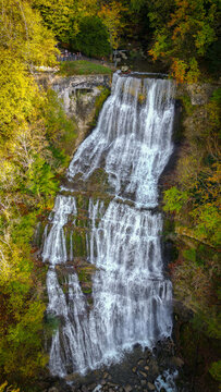 Aerial view of Cascades du Herisson waterfall cascading down rocky cliffs surrounded by autumn forest with vibrant foliage in Le Frasnois, Bourgogne-Franche-Comte, France.