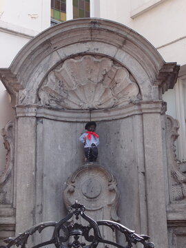 Manneken Pis bronze statue dressed in costume inside stone alcove 