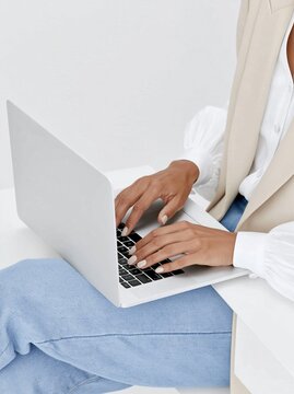 Close-up of a woman typing on a laptop in a bright minimalist home office setting.