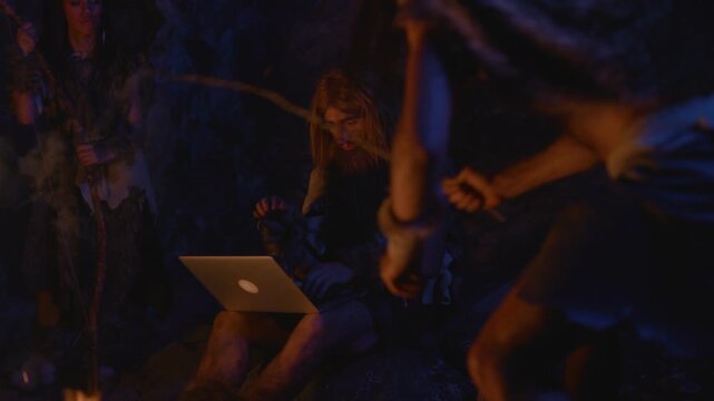 A modern caveman utilizing a laptop while seated around a warm and inviting campfire
