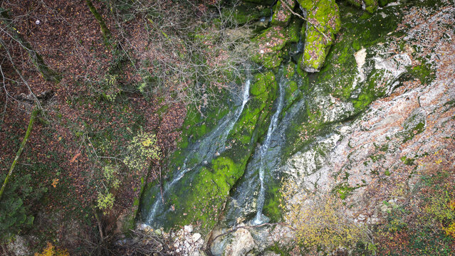 Aerial view of La Source de l'Allondon featuring a cascading stream flowing over mossy rocks surrounded by autumn foliage in Echenevex, Auvergne-Rhone-Alpes, France.