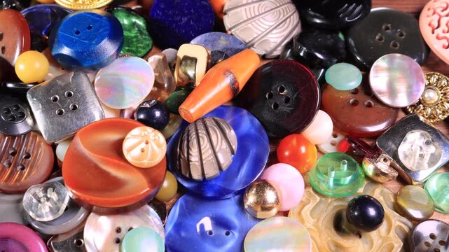 Densely packed pile of mismatched vintage buttons varying in size, shape, color, texture and finish, viewed from above. Panning shot