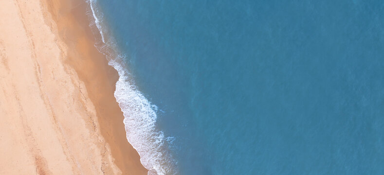 Aerial drone view of turquoise ocean waves washing onto a sandy tropical coastline. Minimal beach background with generous copy space, ideal for travel advertising, summer campaigns, tourism branding,