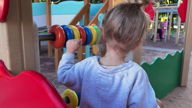 Young child playing with a large educational abacus structure in a colorful outdoor playground