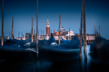 Iconic postcard cityscape parked gondolas against ancient cathedral bell tower at night, Venice, Italy © Igor
