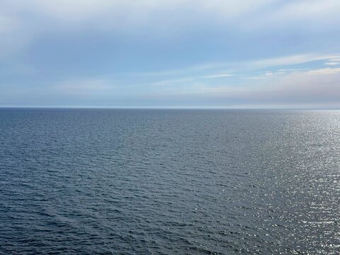 Open ocean calm shiny water and cloudy sky horizon.