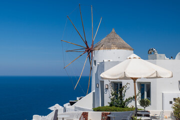 Traditional Santorini windmill with umbrellas and bright blue sea under clear summer sky in Oia, Greece. © Andrei Tomas