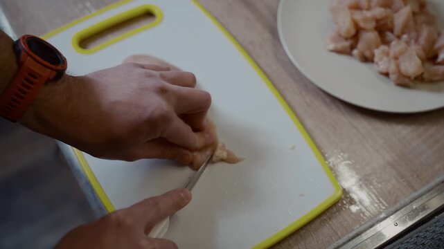 Process of cooking chicken breast in kitchen with knife. Young husband helps his wife in the kitchen, cuts fresh chicken breast meat on a white plastic board. Cooking healthy food, dietary poultry.