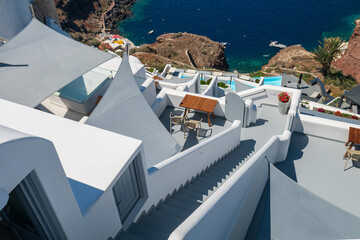 Sunlit Cycladic architecture with rooftop terrace, steps, and deep blue Aegean water in Santorini, Greece. © Andrei Tomas