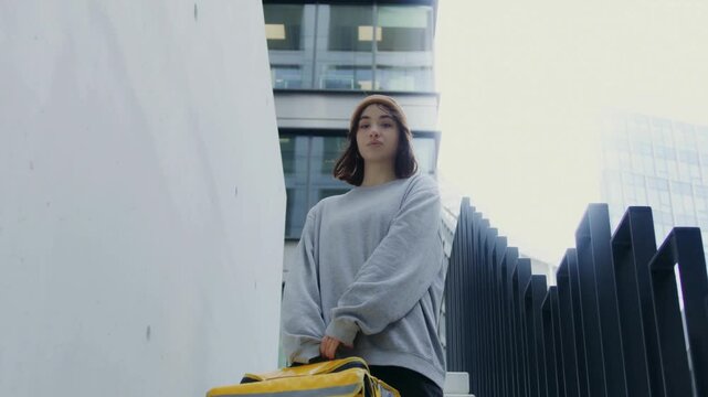 Young courier walking down outdoor stairwell carrying yellow delivery bag in housing complex