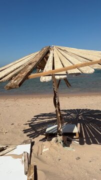 Abandoned wooden beach umbrella made of planks, weathered, tilted, offering no shade under harsh sun.