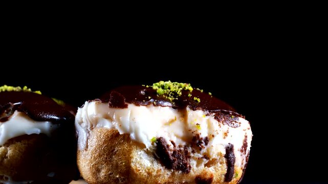 Delicious chocolate cream puffs with pistachio topping isolated on a dark black background for food marketing.
