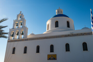 Whitewashed Greek Orthodox church facade with blue dome and belfry against clear sky on Santorini island, Greece. © Andrei Tomas