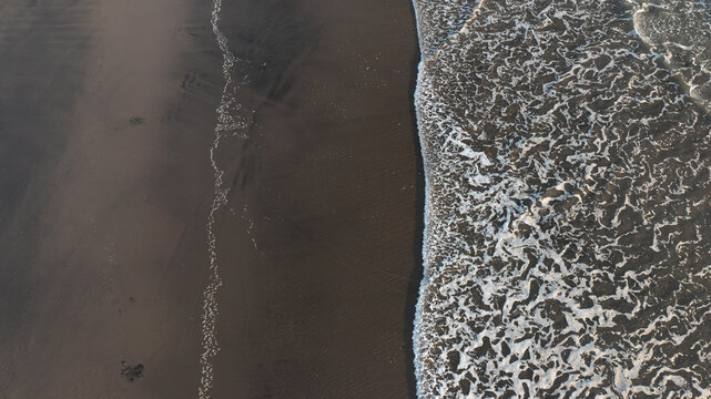 Aerial view of the dark black sand beach and white sea foam of the ocean waves at Piha, Auckland, New Zealand.