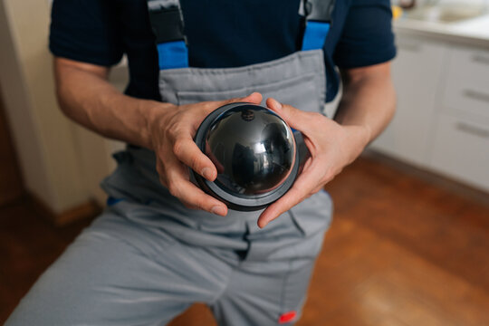 Technician in uniform holding dome surveillance camera. Close-up on hands installing home security system equipment. Concept of safety, protection, monitoring professional service.