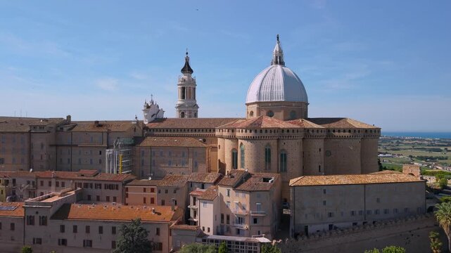 Loreto Marche Italy 4K Aerial. Drone backward reveal of historic fortified town with basilica dome. Authentic Italian borgo on hilltop surrounded by green fields with blue sea background. Hidden gems