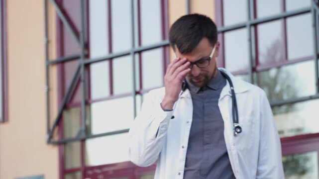 Stressed out doctor. Male medic taking glasses off to rest her eyes and relax from work. Adult man doctor working long hours. It's hard work saving lives. Doctor in lab coat rubbing his eyes.