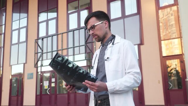 Medicine and healthcare theme. Medical student examines a CT scan of lungs outside the university entrance. Young medical worker examining x-rays of a coronavirus patient. Doctor analyzes mri scan.