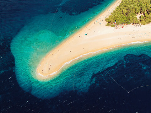 Aerial view of Golden Horn Beach with its iconic pebble spit extending into the turquoise Adriatic Sea, surrounded by pine trees and clear blue water in Bol, Split-Dalmatia County, Croatia.