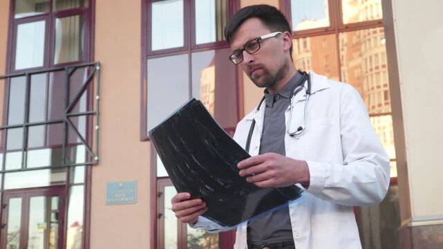 Medicine and healthcare theme. Medical student examines a CT scan of lungs outside the university entrance. Young medical worker examining x-rays of a coronavirus patient. Doctor analyzes mri scan.