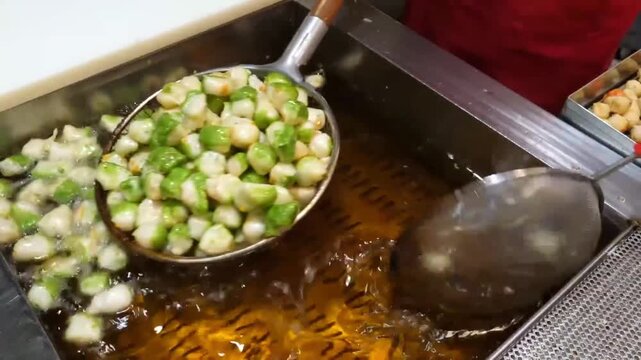 Close-up of a street food vendor deep frying small, bite-sized Korean fish cakes (Eomuk) in a large vat of hot oil. The footage captures the bubbling oil and the vendor using a metal strainer to stir 
