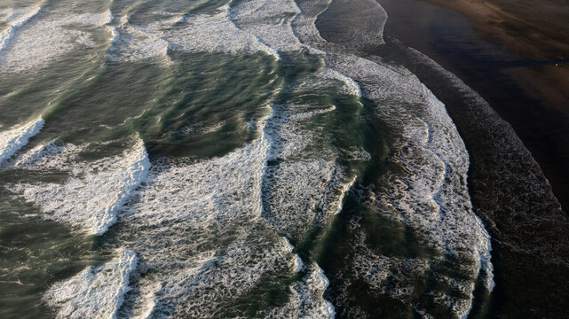 Aerial view of the dark sand and powerful surf at Piha Beach with white foam patterns on the water in Piha, Auckland, New Zealand.