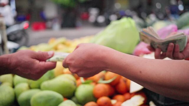 Vietnam street fruit seller exchanging cash with customer over pile of mangoes and mandarins during busy roadside market transaction sequence