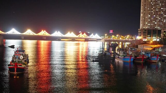 Illuminated cable-stayed bridge over river at night with moored fishing boats