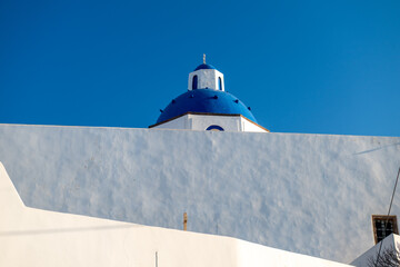 Whitewashed Cycladic church with blue dome in Santorini, Greece, captured in bright daylight with minimalist architecture and copy space. © Andrei Tomas