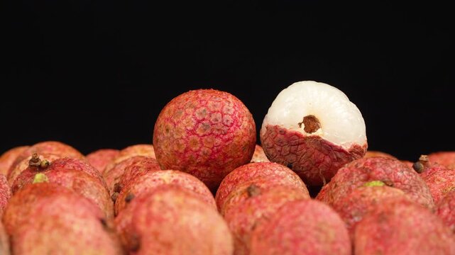 Macro shot of a peeled lychee with white pulp and a whole fruit rotating on a black background