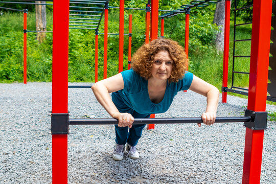 Middle-aged woman doing outdoor fitness workout on parallel bar at a park calisthenics area