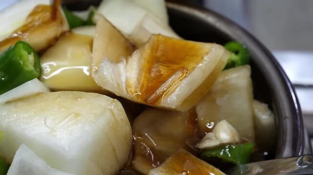 A detailed close-up shot of a chef or home cook preparing traditional Korean fish cake stir-fry, known as Eomuk Bokkeum or Odeng Bokkeum. The footage shows bite-sized pieces of chewy fish cakes being 