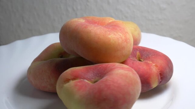 Close-up of a pile of flat donut peaches rotating on a white turntable, showcasing their unique shape and fuzzy skin under bright studio lighting.