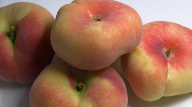 Close-up of a pile of flat donut peaches rotating on a white turntable, showcasing their unique shape and fuzzy skin under bright studio lighting.