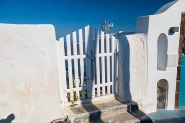 Sunlit white plaster walls and wooden gate against clear blue sky on Santorini, Greece. © Andrei Tomas