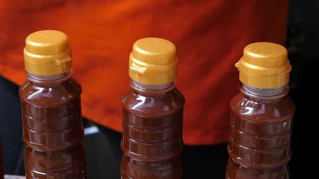 Close-up of a person's hand opening a small plastic bottle filled with thick, red spicy sauce typically used for Korean stir-fried fish cakes (Eomuk Bokkeum) or street food skewers.