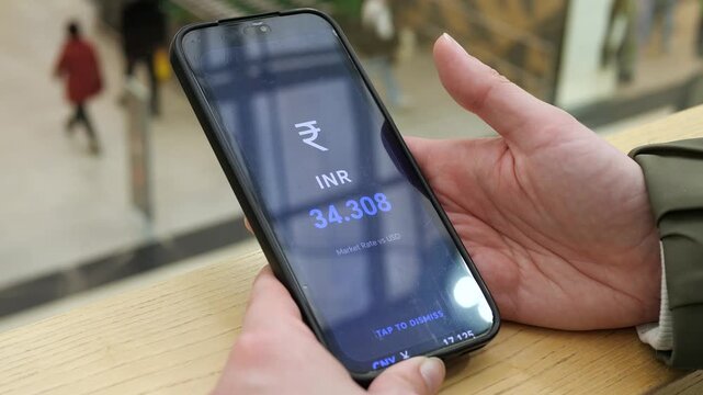 User checking the live INR to USD exchange rate on a mobile device. Large blue digits display 34.308. Ideal for currency trading, Indian finance, and global market updates stock footage.