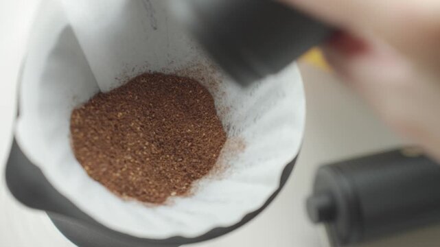 Coffee grounds being added to paper filter inside coffee dripper during pour over setup. Concept of manual brewing and fresh coffee preparation
