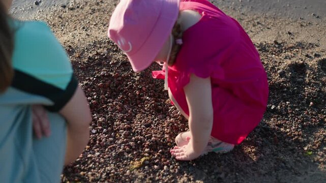 Little girl in pink dress and bucket hat blowing soap bubbles on sandy beach. Child playing with bubble wand outdoors during sunny summer day. Childhood fun.