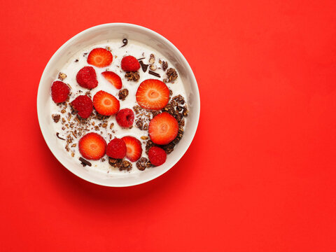 Luxurious chocolate muesli with sliced strawberry, raspberry and milk in a round bowl on bold red surface. Excellent breakfast healthy food option.. Great for food blogs. Vivid colors.