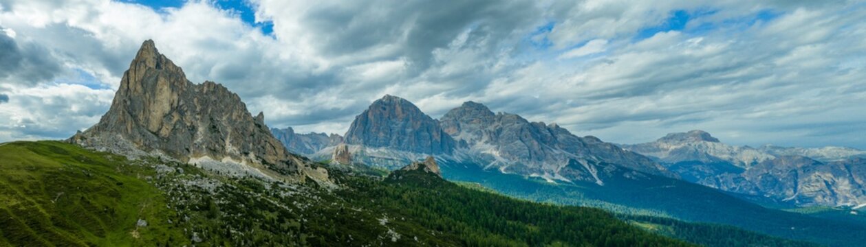 Dramatic panorama of Ra Gusela and Passo Giau beneath stormy clouds in the Italian Dolomites. Sunlit alpine meadows contrast with rugged limestone peaks and moody mountain scenery.