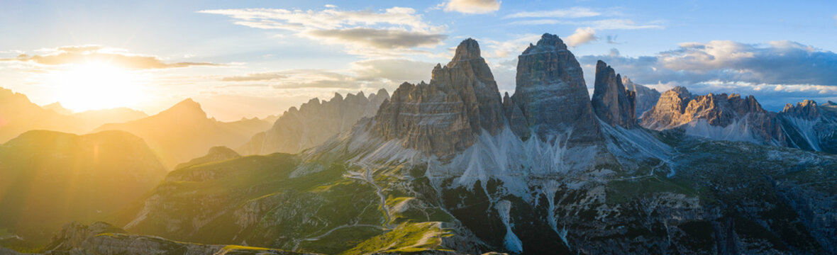 Panoramic view of Tre Cime di Lavaredo glowing in golden sunset light in the Italian Dolomites. Dramatic alpine landscape with rugged peaks, winding trails and breathtaking scenery.