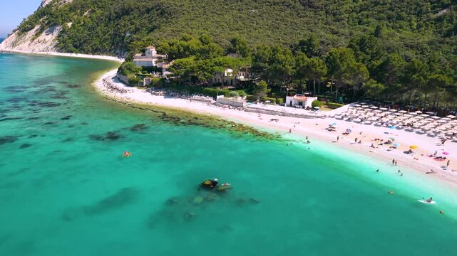 Portonovo Italy 4K Aerial. Drone flight from Romanesque church over white beach with canoes in turquoise sea. Authentic Marche hidden gems coastline. Secret travel paradise establishing landscape
