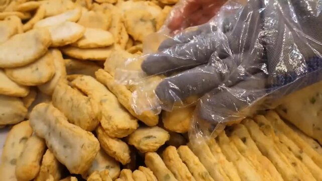 A close-up shot of a street food vendor wearing plastic gloves, carefully arranging freshly deep-fried Korean fish cake bars (Eomuk or Odeng) into a metal tray at a bustling market in South Korea. The
