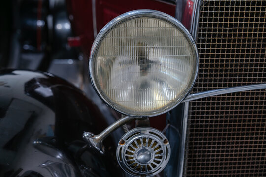 Detailed close up of a vintage headlight and horn mounted on a classic automobile. The image highlights antique automotive craftsmanship and chrome accents.