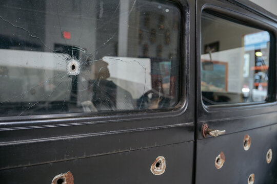 Vintage automobile door featuring bullet holes and a cracked window. The historic vehicle displays visible damage and weathered metal surfaces.