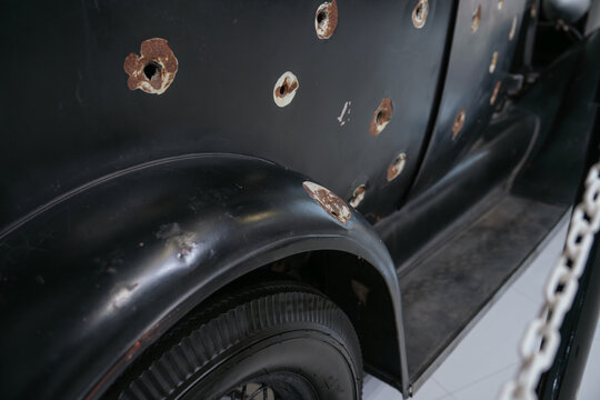 Close up of multiple bullet holes on the body of a vintage automobile. The historic vehicle displays visible battle damage and weathered metal surfaces.