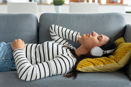 Beautiful woman listening to music with headphones while lying on the couch at home