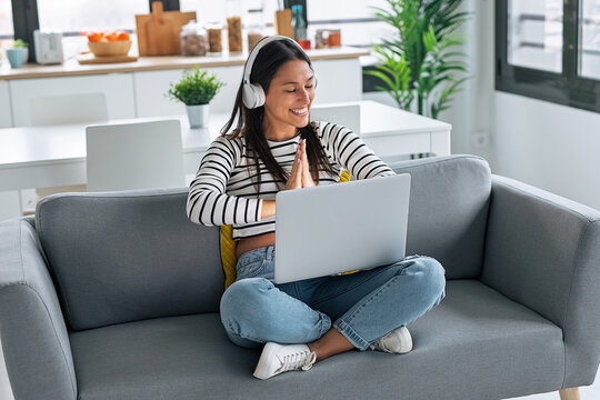 Smiling woman doing meditation while listening to music with headphones sitting on the couch at home